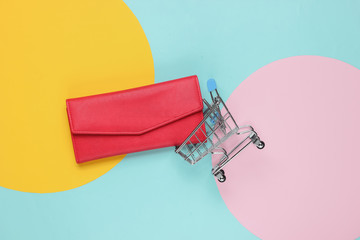 Minimalism shopping concept. Shopping trolley, red leather wallet on color paper background