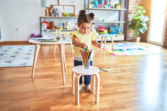 Beautiful toddler standing holding colored pencils at kindergarten