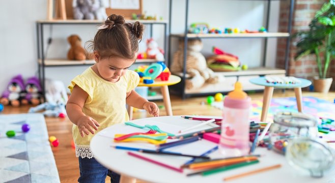 Beautiful toddler standing holding colored pencils at kindergarten