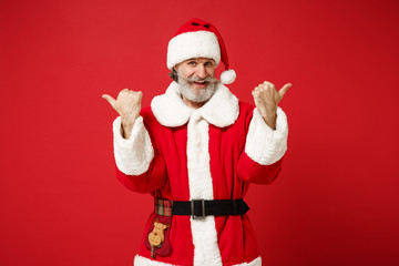 Fototapeta na wymiar Cheerful elderly gray-haired bearded mustache Santa man in Christmas hat posing isolated on red background. Happy New Year 2020 celebration holiday concept. Mock up copy space. Pointing thumbs aside.
