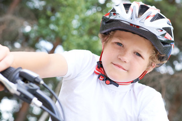 Low angle view of a smiling young boy in safety helmet riding bicycle at the park in summer.