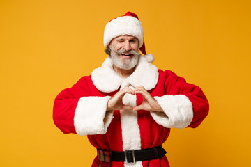 Funny elderly gray-haired mustache bearded Santa man in Christmas hat posing isolated on yellow background. Happy New Year 2020 celebration concept. Mock up copy space. Showing shape heart with hands.