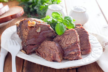 sliced baked beef fillet on a white dish with fresh herbs, horizontal