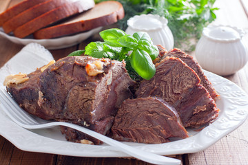 sliced baked beef fillet on a white dish with fresh herbs, horizontal
