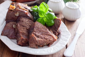 sliced baked beef fillet on a white dish with fresh herbs, horizontal