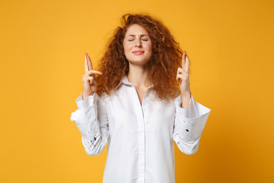 Young redhead woman girl in shirt posing isolated on yellow orange background. People lifestyle concept. Mock up copy space. Wait for special moment, keeping fingers crossed, eyes closed, making wish.