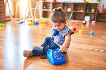 Beautiful toddler sitting on the floor playing with vintage phone at kindergarten