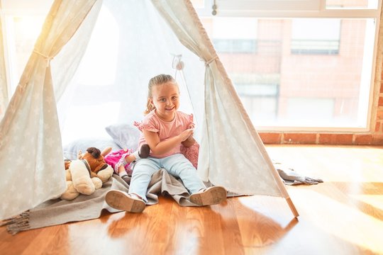 Beautiful blond toddler girl playing with dolls inside tipi at kindergarten