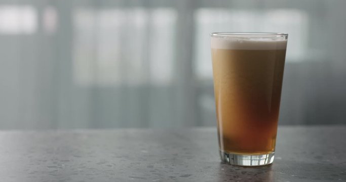 Slow motion nitro light ale beer with beautiful foam in pint glass on terrazzo countertop with window on background