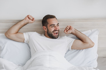 Calm young handsome bearded man lying in bed with white sheet pillow blanket in bedroom at home....