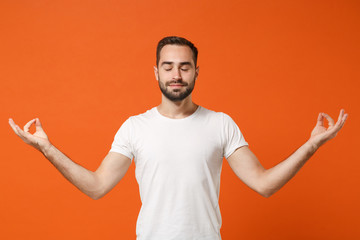 Fototapeta na wymiar Young man in casual white t-shirt posing isolated on orange background in studio. People lifestyle concept. Mock up copy space. Hold hands in yoga gesture, relaxing meditating, keeping eyes closed.