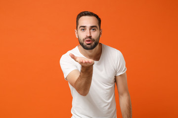 Attractive young man in casual white t-shirt posing isolated on bright orange wall background,...