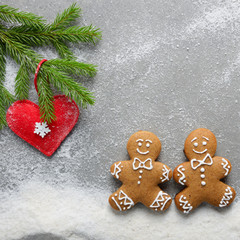 Flat lay at two gingerbread men having a walk on snow under fir twig with handmade heart