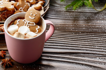 Pink mug with hot chocolate marshmallows and gingerbread man on background of spruce branch and tray with cookies