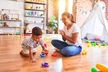 Fototapeta premium Beautiful teacher and toddler boy building pyramid with hoops bolcks at kindergarten