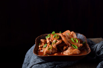Pieces of meat stewed in tomato sauce with spices served in a clay bowl against black background