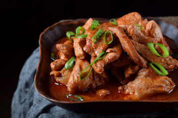 Pieces of meat stewed in tomato sauce with spices served in a clay bowl against black background