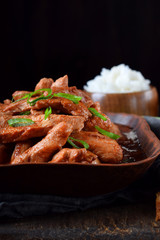 Pieces of meat stewed in tomato sauce with spices served in a clay bowl against black background