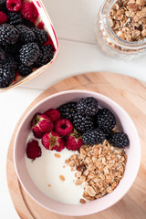 Breakfast with yogurt, berries and granola on a light background.
