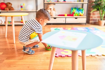 Beautiful toddler boy playing meals with plastic plates, fruits and vegetables at kindergarten