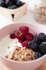 Breakfast with yogurt, berries and granola on a light background.