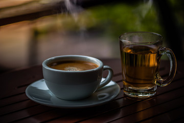 Hot black coffee with white smoke in a white cup, placed on a white saucer on a brown table in a coffee shop.