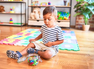 Beautiful toddler boy sitting on puzzle eating small colored chocolate balls at kindergarten