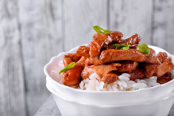 Pieces of meat in tomato sauce with spices on rice in a white bowl