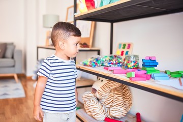 Beautiful toddler boy standing at kindergarten with lots of toys