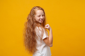 Side view of little ginger kid girl 12-13 years old in white t-shirt isolated on bright yellow background. Childhood lifestyle concept. Mock up copy space. Doing winner gesture, keeping eyes closed.