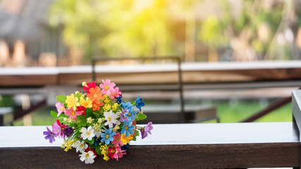 Variety of colorful plastic flowers on a wooden table blurred background
