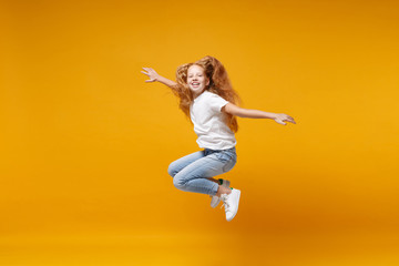 Fototapeta na wymiar Pretty little ginger kid girl 12-13 years old in white t-shirt isolated on yellow background. Childhood lifestyle concept. Mock up copy space. Having fun, fooling around, jumping, spreading hands.