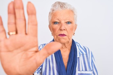 Senior grey-haired woman wearing blue striped shirt standing over isolated white background with open hand doing stop sign with serious and confident expression, defense gesture