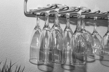 Black and white photo of group of transparent wine glasses with beautiful reflections hanging up on a gray metal shelf