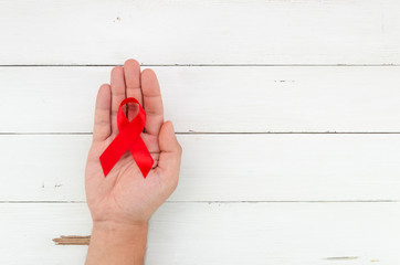 AIDS ribbon in male hand on white wooden planks background with space for text. December first World AIDS Day concept