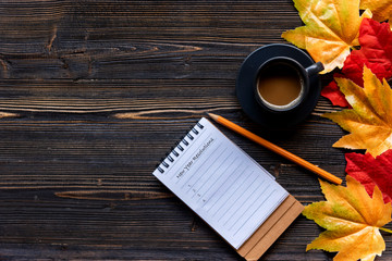 New Year Resolutions Conceptual. Seasonal autumn maple leaves.  Cup coffee hot steaming  warm scarf with paper note for greeting text on wooden table background in morning relax sunny day. 