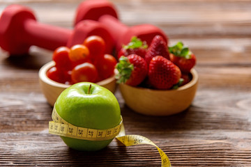 Diet and weight loss with green apple with measuring tap and fitness equipment, fresh fruits salad healthy on wooden background top view.  Healthy Concept.