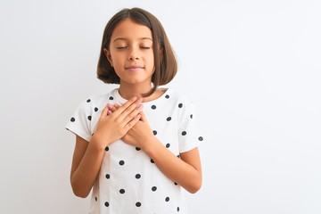 Young beautiful child girl wearing casual t-shirt standing over isolated white background smiling with hands on chest with closed eyes and grateful gesture on face. Health concept.