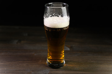 Photo of beer in a glass. Thick foam and a nice color drink on a black background.