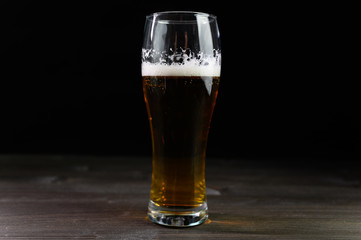 Photo of beer in a glass. Thick foam and a nice color drink on a black background.