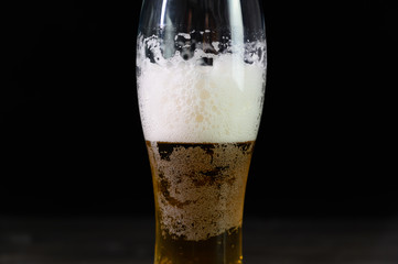 Photo of beer in a glass. Thick foam and a nice color drink on a black background.