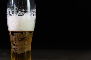 Photo of beer in a glass. Thick foam and a nice color drink on a black background.