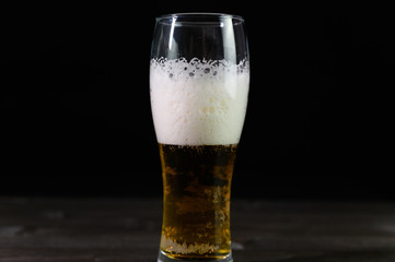 Photo of beer in a glass. Thick foam and a nice color drink on a black background.