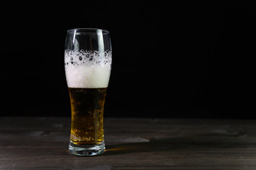 Photo of beer in a glass. Thick foam and a nice color drink on a black background.
