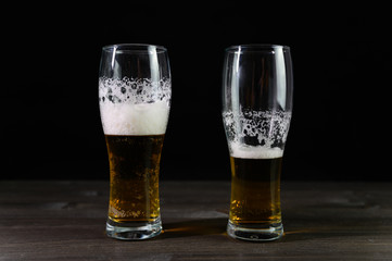 Photo of beer in two glasses. Thick foam and a nice color drink on a black background.