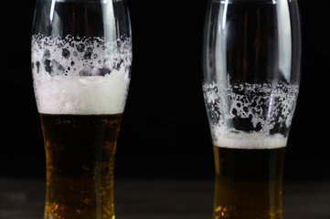 Photo of beer in two glasses. Thick foam and a nice color drink on a black background.