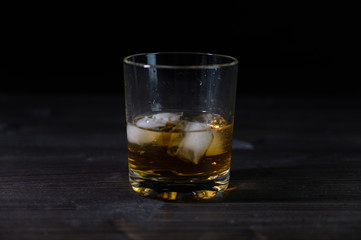 Photo of whiskey in a glass with ice. Real ice and a pleasant color of the drink on a black background.