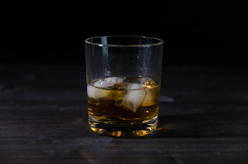 Photo of whiskey in a glass with ice. Real ice and a pleasant color of the drink on a black background.