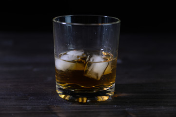 Photo of whiskey in a glass with ice. Real ice and a pleasant color of the drink on a black background.