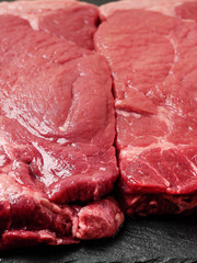Raw uncooked sirloin steak, on a black slate plate, meat cut and preparation.